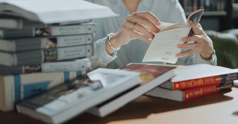 A young adult reading a book amidst a stack of books in a library, focusing on self-education and study.