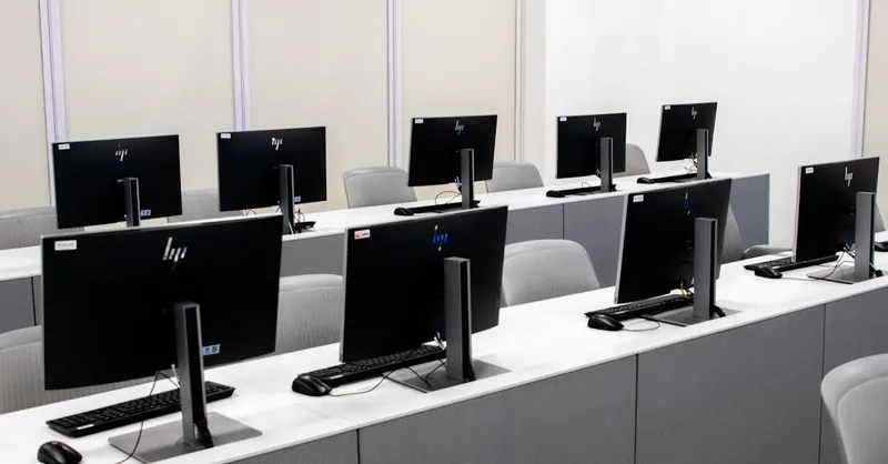 An empty computer lab with modern desktop setups and ergonomic chairs.