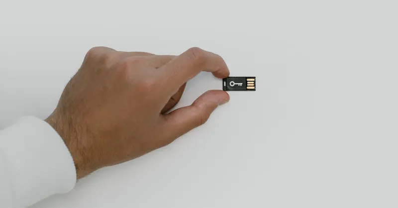 Close-up of a hand holding a USB flash drive with a key symbol, signifying digital security.