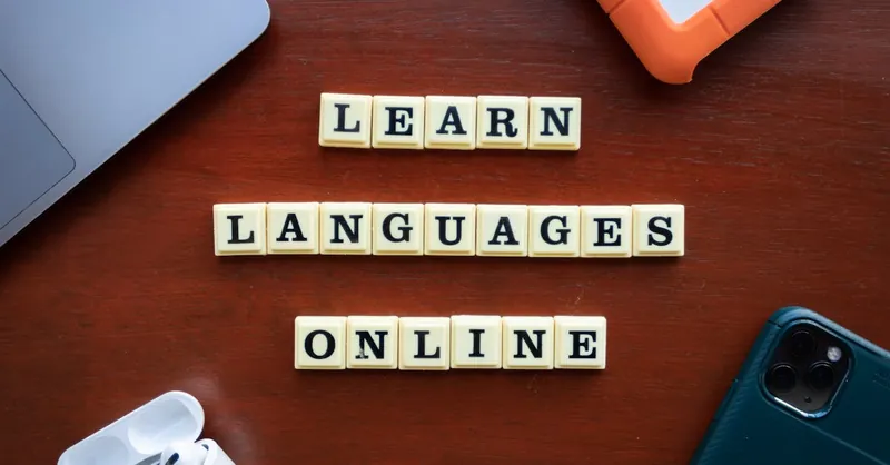 Flat lay of language learning tools with devices and text blocks on desk.
