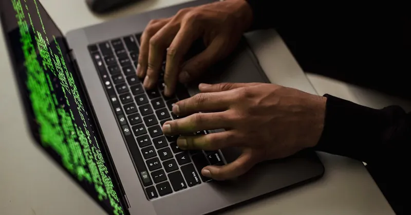 From above of crop anonymous male hacker typing on netbook with data on screen while sitting at desk