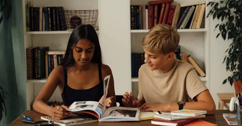 Two teenagers reading books at home, showcasing diversity and learning.