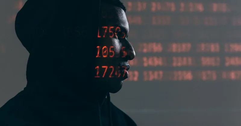 Side profile of a man in a hoodie, surrounded by red code, depicting cybersecurity theme.