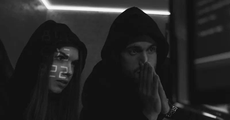 Two cybersecurity experts in hoodies study data on screens in a dimly lit room, symbolizing cyber defense.